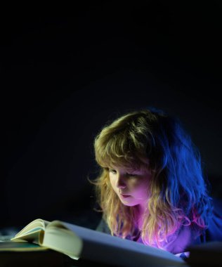 Çocuk karanlık odada masal okuyor. Küçük bir çocuk karanlık evde kitap okuyor. Çocuklar gece lambasıyla yüz yüze.