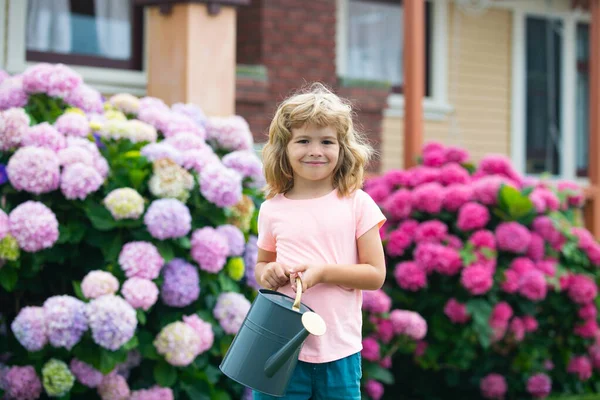 Bahçede sulama tenekesiyle çiçekleri sulayan sevimli küçük çocuk. Hafif yaz kapakları ve renkli tişörtler giymiş, gülümseyen ve eğlenen bir çocuk. Çocuklarla açık hava aktiviteleri.