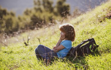 Çocuklar yüksek çayırlarda oturuyor ve dağların ve doğanın güzel manzarasına hayran kalıyorlar. Küçük bir oğlan ve küçük bir kız çimlerde, dağ sıralarında ve orman arka planında..