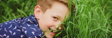 Bahar çocuğu suratlı pankart. Çimen geçmişi olan gülümseyen çocuk. Sahada eğlenen tatlı bir çocuk. Doğayla birlik. Yeşil çim arka plandaki çocuklar.