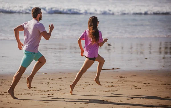 Sportsman and sportswoman running together by the sea. Couple running on beach.