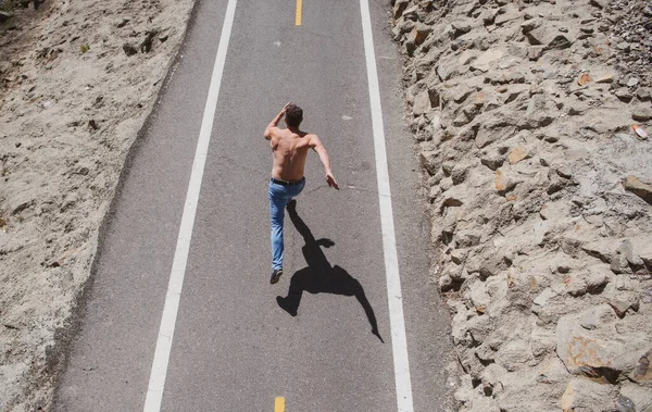 Achteraanzicht van een hardloper die jogt op de weg. Fit mannelijke madel workout met kale romp op stedelijke straat. — Stockfoto