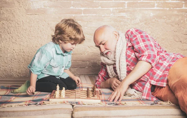 Hombre maduro con niño jugando al ajedrez. Jaque mate. Lindo niño jugando al ajedrez. Infancia. Concepto de abuelo y nieto. Ajedrez pieza. — Foto de Stock