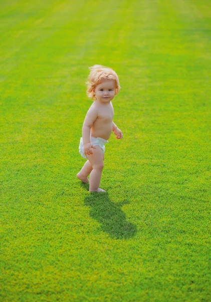 Gelukkige baby in gras op de fieald 's zomers avond. Glimlachend kind draagt een luier buiten. Gelukkige kindertijd en kinderzorg. — Stockfoto