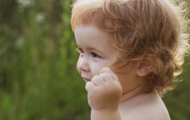 Küçük çocuk parkta oynuyor. Çim tarlasında mutlu bir bebeğin portresi. Bebek yüzlü, yakın çekim. Küçük komik çocuk portresi. Sarışın çocuk, duygusal yüz..