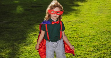 Kahraman Çocuk dışarıda eğleniyor. Süper kahraman küçük çocuk yeşil arka planda.