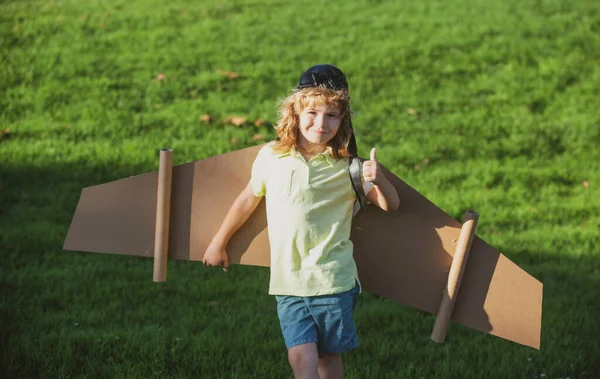 Barn flyger. Rolig pojke med tummen upp leende bära pilot hatt och glasögon flyger med leksak kartong flygplan vingar, Starta frihet koncept, bekymmersfri unge. — Stockfoto