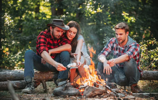 Группа туристов отдыхает у костра. Друзья проводят выходные на фоне лесной природы. Туристы расслабляются. Счастливая молодежь отдыхает в лесу. Веселые мужчины и женщины устраивают пикник . — стоковое фото