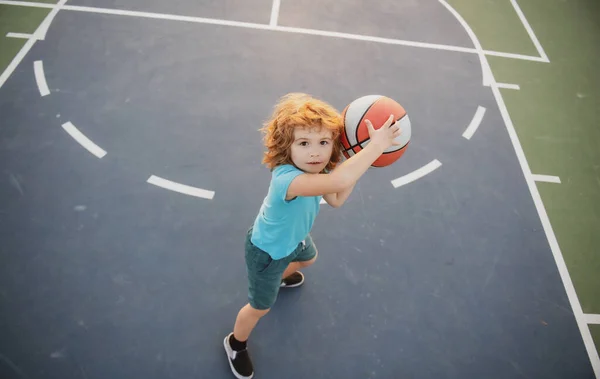 Bonito menino sorrindo joga basquete. Crianças ativas desfrutando de jogo ao ar livre com bola de cesta, vista superior. — Fotografia de Stock