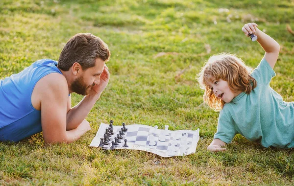 Father and son playing chess lying on grass at lawn park. Fathers Day, love family, parenthood, childhood concept. — Stock Photo, Image