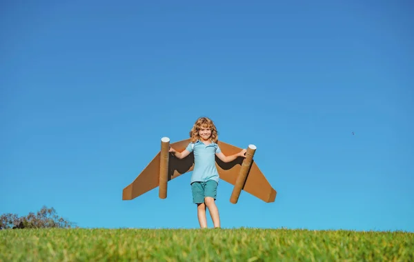 Парень с игрушечным реактивным ранцем на открытом воздухе. Ребенок играет на зеленом весеннем поле с картонными крыльями. Весенние путешествия и приключения. Успех и лидерство детей, концепция запуска. — стоковое фото