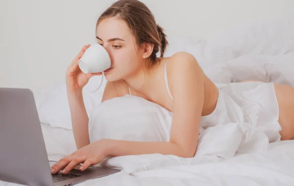 Giovane donna che si diverte a letto sul soggiorno con caffè e laptop. — Foto Stock