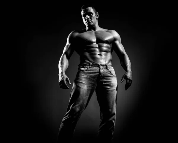 Sexy beau bronzé homme caucasien en jeans, debout torse nu, montrant six pack abdos abdominaux, ont un corps parfait, fond noir foncé. — Photo