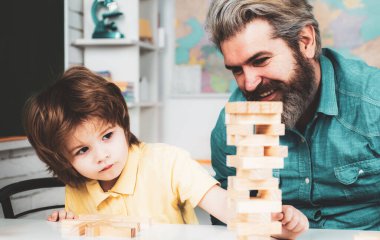 Educational games. Smiling father and focused son playing jenga game at home.