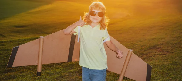 Pojkbarn drömmer och reser. Pojke med flygplansleksak vid solnedgången utomhus. Glada barn leker med leksaksflygplan utomhus på sommarfältet. Resor, semester och frihet koncept. — Stockfoto