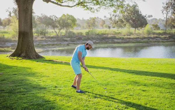 Golfista gra w golfa na wieczornym polu golfowym. Golfista z kijem golfowym strzela. — Zdjęcie stockowe