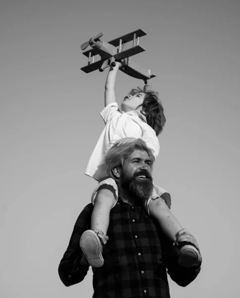 Día de los Padres. Padre e hijo. Niño con juguete avión sentado en los hombros de los padres en el cielo. — Foto de Stock