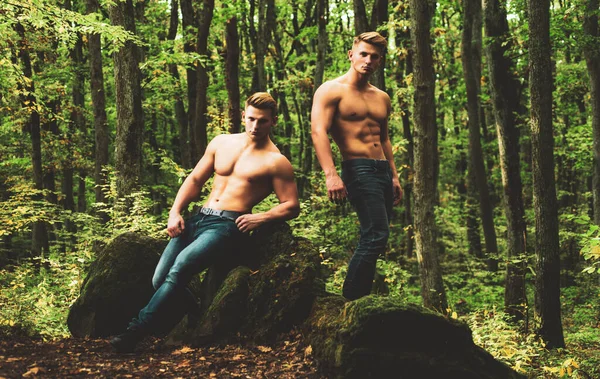 Homens sexy com corpo muscular e tronco nu e calças jeans. Retrato de moda de jovens rapazes nus quentes na floresta. Comprimento total, natureza fora. — Fotografia de Stock