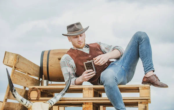 Cowboy farmer vidéken nyugati cowboy kalapot visel. Amerikai férfi modell vidéken. Vonzó férfi whiskyvel vagy brandyvel.. — Stock Fotó