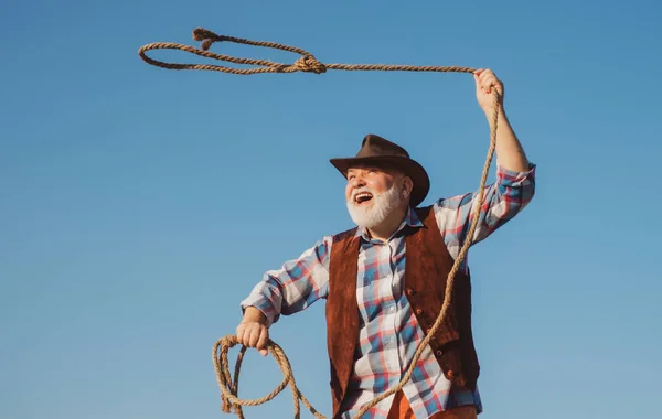 Old wild west cowboy with rope. Bearded western man throwing lasso with brown jacket and hat catching horse or cow. — Foto de Stock