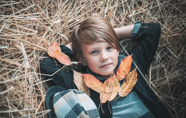 Jongen ligt op het hooi. Schattige kleine kind jongen houdt van bladgoud op boerderij dorp achtergrond. Schattige kleine jongen bereiden zich voor op zonnige herfstdag. — Stockfoto