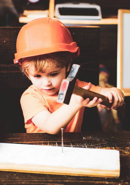 Child with helmet in orange hard hat. Tools construction. Boy hammering. Kid hammers nail. — Stock Photo, Image