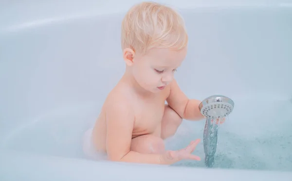 Lustiger blonder Junge, der Spaß mit Wasser hat, indem er in der Badewanne badet. Hygiene und Betreuung von Kleinkindern. — Stockfoto