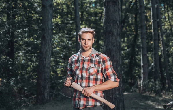 Un joven guapo con barba lleva un árbol. Joven elegante haciéndose pasar por leñador. Trabajador de madera caminando en el bosque con hacha. —  Fotos de Stock
