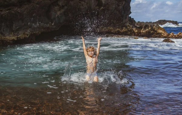 Criança levanta as mãos na água e espirra gotas de água no mar. Crianças férias de verão e conceito de viagem. — Fotografia de Stock