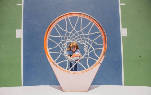 Jogo de basquetebol. Bonito menino segurando uma bola de basquete tentando fazer uma pontuação. — Fotografia de Stock