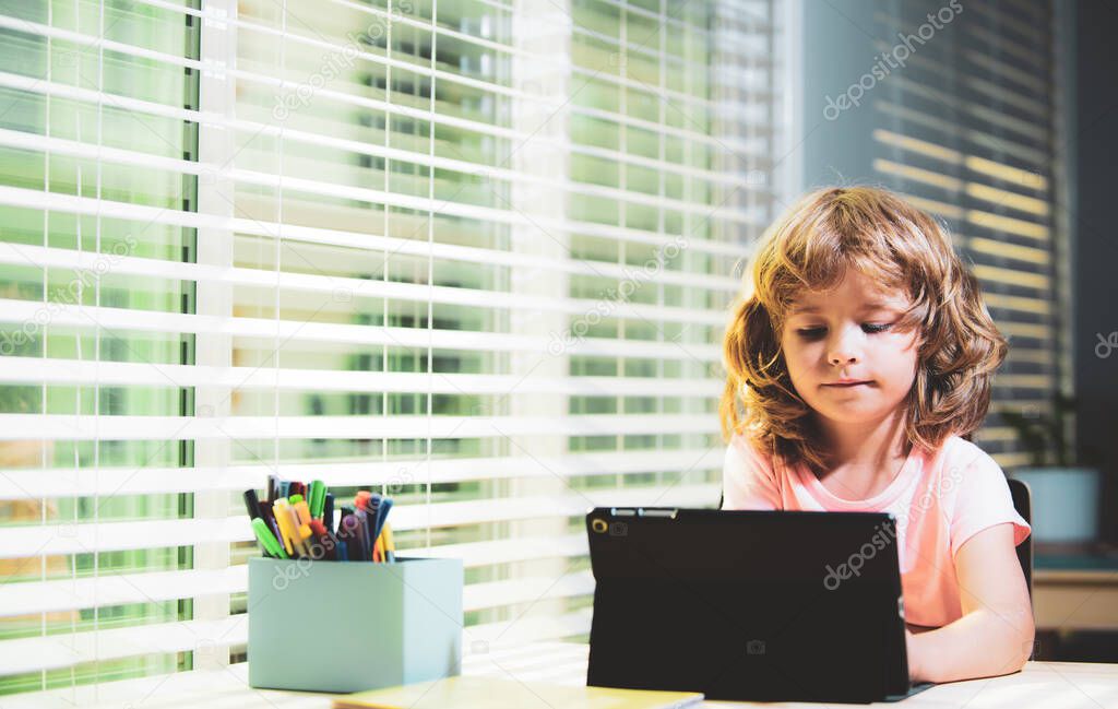 Cute kid boy using tablet on desk at home. Online education concept. Kids education, knowledge.