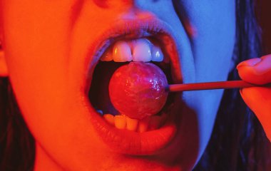 Cazibeli ağız kırmızı dudaklı lezzetli lolipopları yalıyor. Lolipop berbat. Seksi kadın dudağı. Lolipopu olan şehvetli, kırmızı dudaklı bir kadın. Çikolata konsepti.