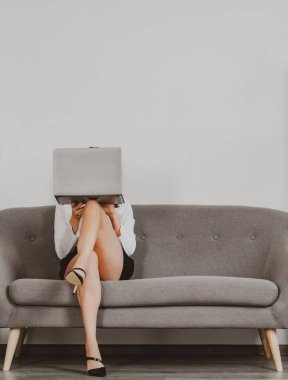 Güzel sekreter bacakları. Seksi bacaklı seksi bir iş kadını. Baştan çıkarıcı kadın yüzünü dizüstü bilgisayarla kapatıyor. Şehvetli sekreter koltukta oturuyor..