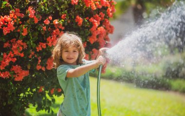Küçük mutlu çocuk ev bahçesinde eğleniyor. Çocuk bahçe hortumunu tutuyor. Hasat zamanı arka bahçede çocuklar için açık hava oyunları.
