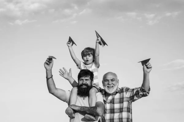 Feliz menino sorridente no ombro pai olhando para a câmera. Família feliz. Aviador piloto infantil com papel avião sonha em viajar. Conceito de geração . — Fotografia de Stock