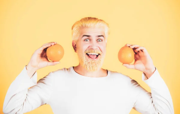 オレンジを手に笑顔で面白い男。ハンサムな若い男は新鮮な天然オレンジを保持します。男楽しみますフルーツリフレッシュオレンジ上のオレンジ背景孤立. — ストック写真