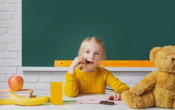 Kisiskolás lány csokoládét eszik az osztályban, angol nyelvet tanul az iskolában. Zseniális gyerek, a tudás napja. Gyerekek oktatás és tudás. — Stock Fotó
