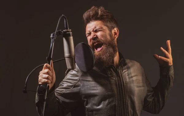 Singing man in a recording studio. Expressive bearded man with microphone. Expressive singer with microphone.
