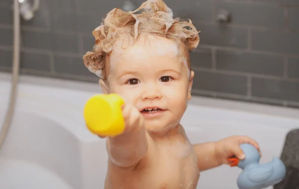 Glad baby tar ett bad och leker med skumbubblor. Ett litet barn i ett badkar. Ett leende barn i badrummet med leksaksanka. Spädbarnstvätt och badning. Barnomsorg och hygien. — Stockfoto