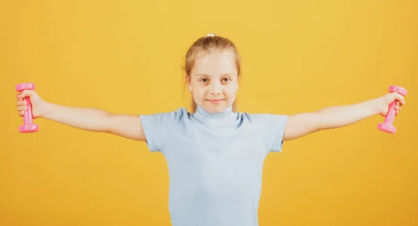 Fitness child. Portrait of sporty little girl with dumbbells over yellow studio isolated background. Gym workout. Child sportsman, childhood activity. Kids sport and Fitness. — Stockfoto