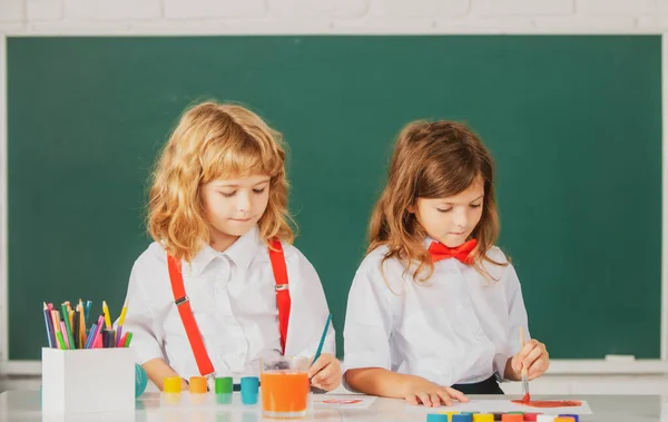 Niños de la escuela niña y niño pintando con pinturas de color y pincel en el aula. Dibujo de hermanos con lápiz y pinturas. — Foto de Stock