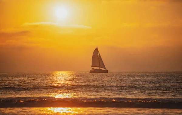 Żaglówka na morzu. Nadmorski złoty wschód słońca nad morzem. Krajobraz natury. Piękny pomarańczowo-żółty kolor na oceanicznym zachodzie słońca. Wybrzeże ze złotym niebem i chmurami. — Zdjęcie stockowe