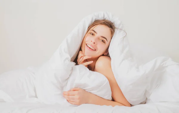 Mujer joven envuelta en una suave manta sentada en la cama. Chica sonriente sentada en la cama y sonriendo en casa. —  Fotos de Stock