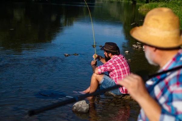 Ung och gammal fiskare står på stranden av sjön med fiskespö. Far och son njuter av livet. Mäns familj, farfar och Drandson fiskar. Gammal man fiskare fira pensionering. — Stockfoto