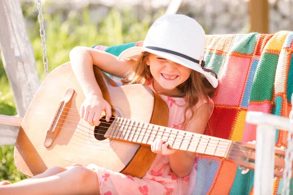 Gitar çalan çocuk müzisyen. Yazlık elbise giyen şık küçük bir kız çocuğu arka bahçede eğleniyor. Sıcak havalarda çocuklar için yaz etkinliği. — Stok fotoğraf