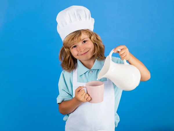 Leite para crianças. Criança cozinheiro chef prepara alimentos em fundo estúdio azul isolado. Crianças a cozinhar. Menino adolescente com avental e chapéu de chef preparando uma refeição saudável de legumes na cozinha. — Fotografia de Stock