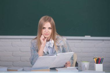 Female college student reading book in classroom, preparing for exam.