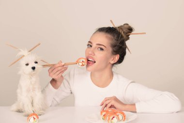 Japon suşi tarzı. El ele tutuşan genç kadın Makizushi suşi rulosu, geleneksel Japon yemekleri izole edilmiş stüdyo portresi. Kadın ve yavru köpek ellerinde çubuklarla suşi yiyorlar..