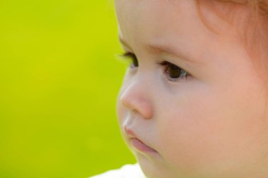 Yaz mevsiminde yeşil çimlerin üzerinde sevimli bebek yüzü. Komik küçük çocuk, yeşil doğanın portresini yakından çek..