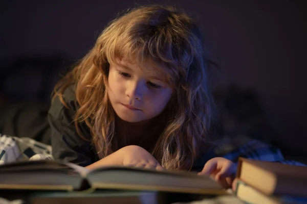 En liten söt pojke som läser en bok som ligger på sängen. Barn utveckling av fantasin. — Stockfoto
